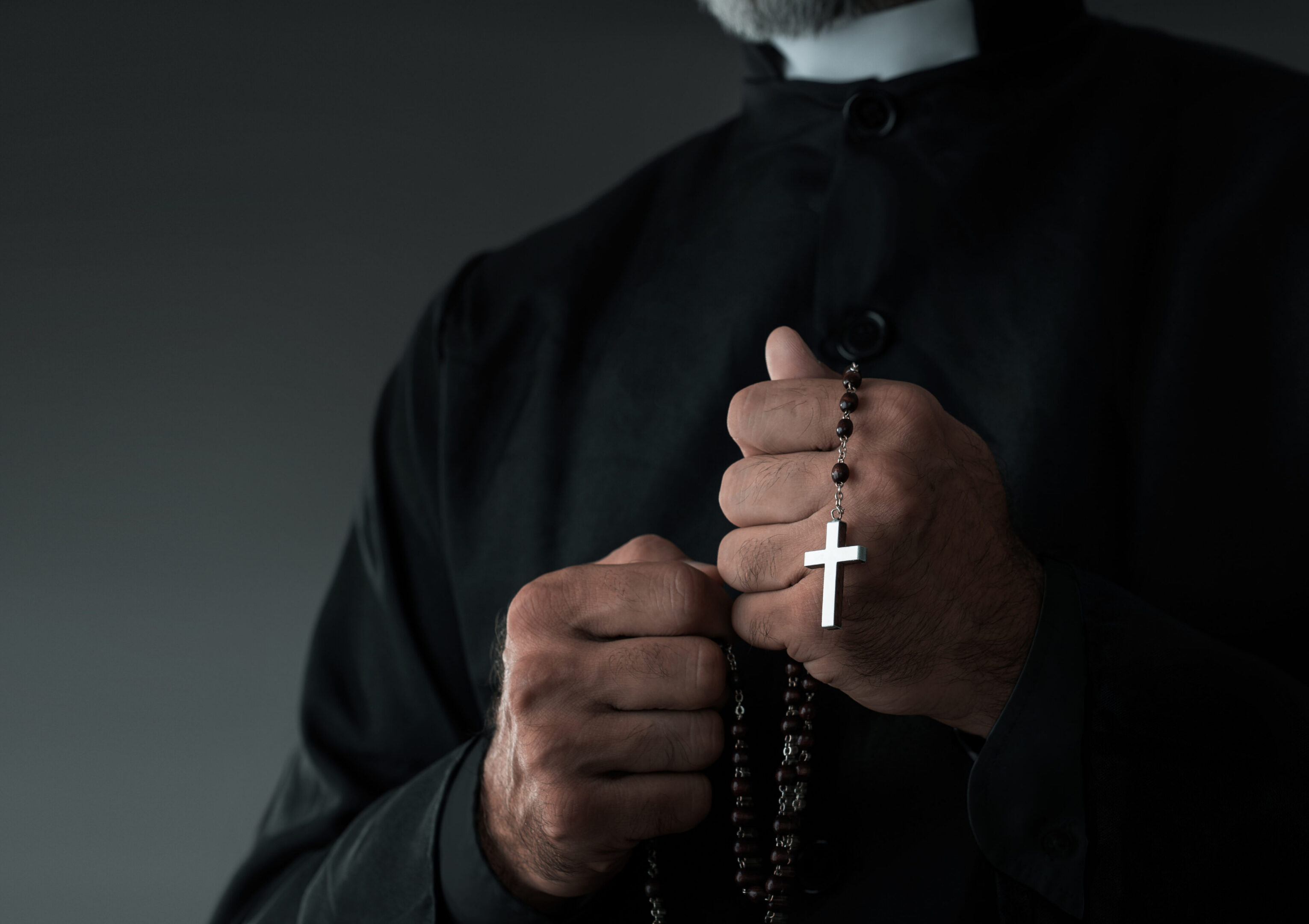 Priest holding rosary beads in hands.