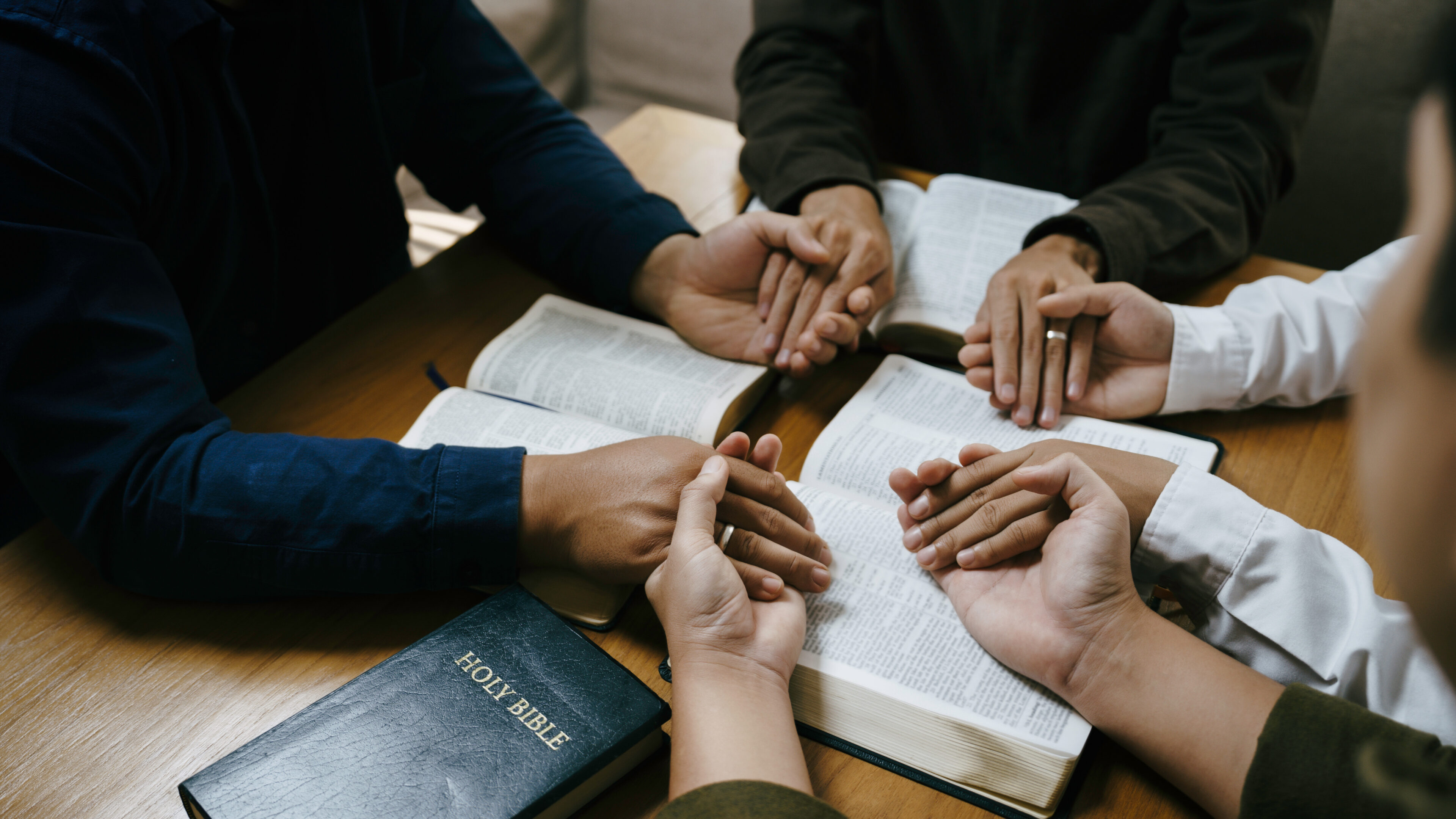 People holding hands in prayer with Bible.