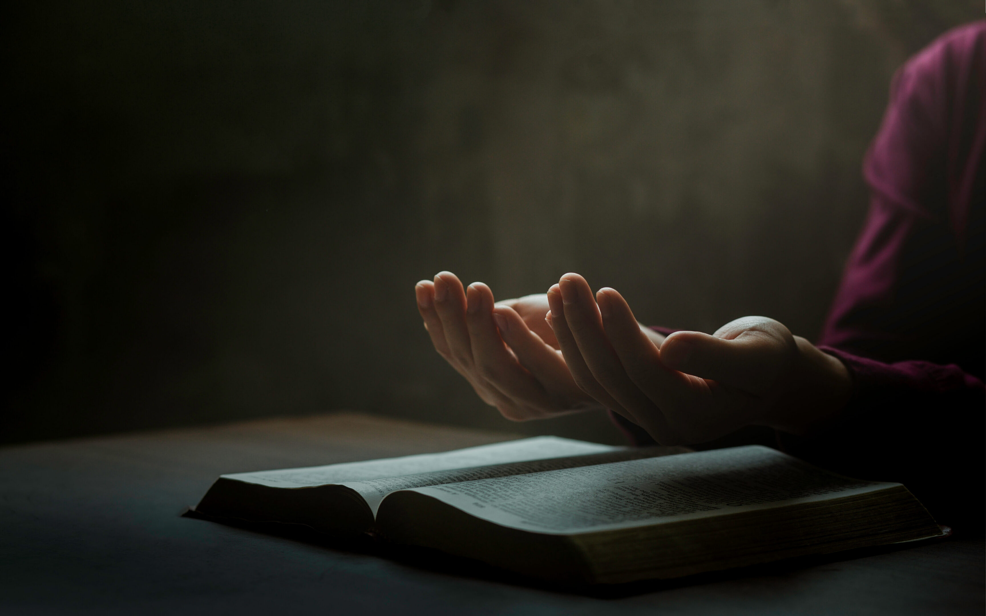 Hands praying over an open book.