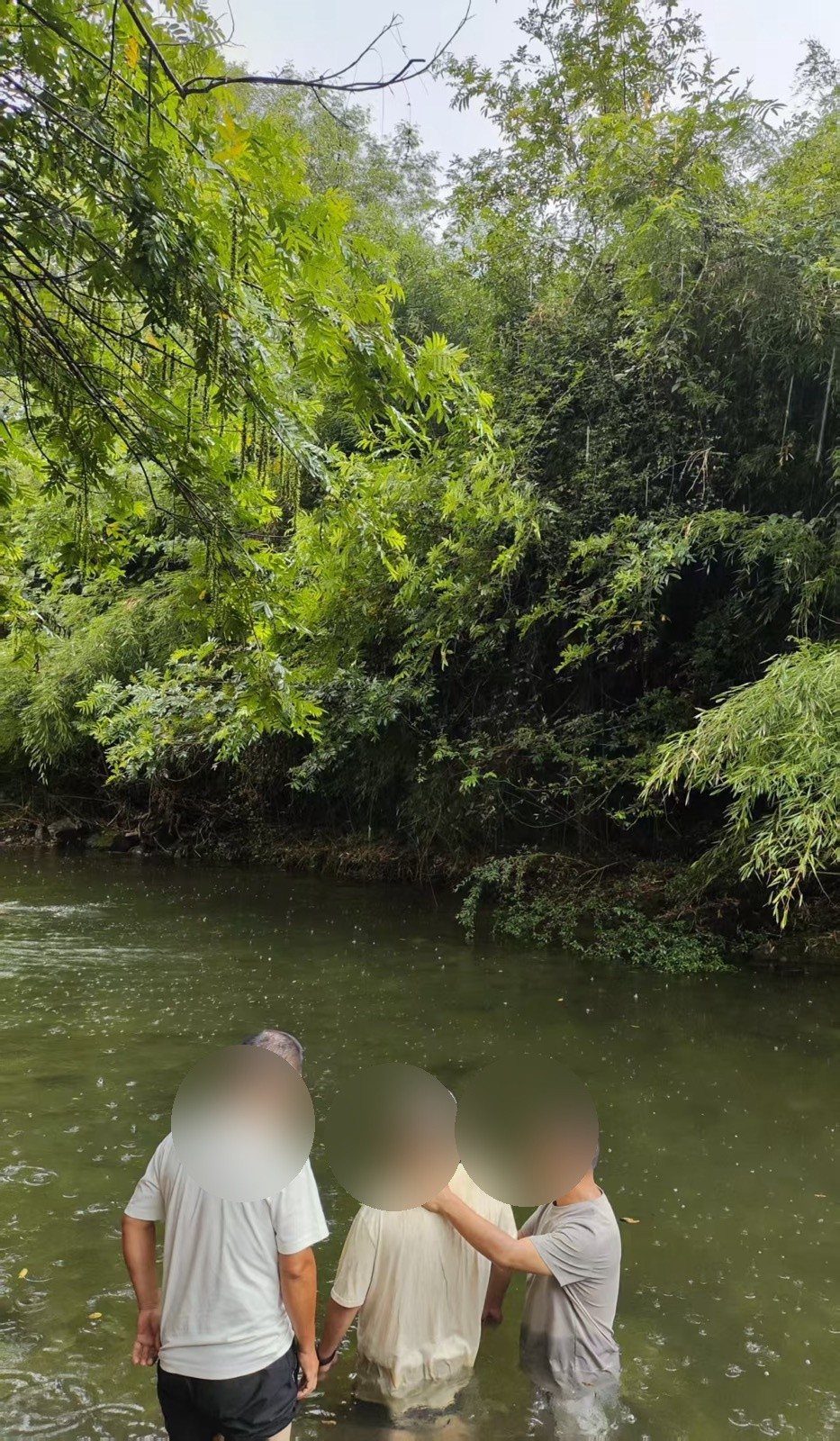 Three people in a river during a baptism, with faces blurred